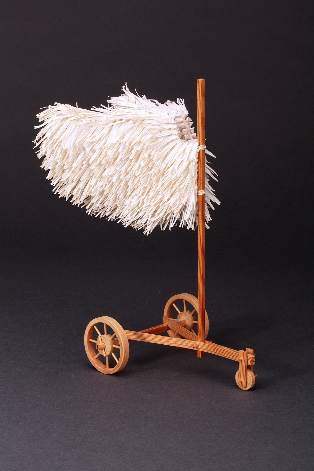 A wooden structure with three wheels and a vertical post supports two wings.