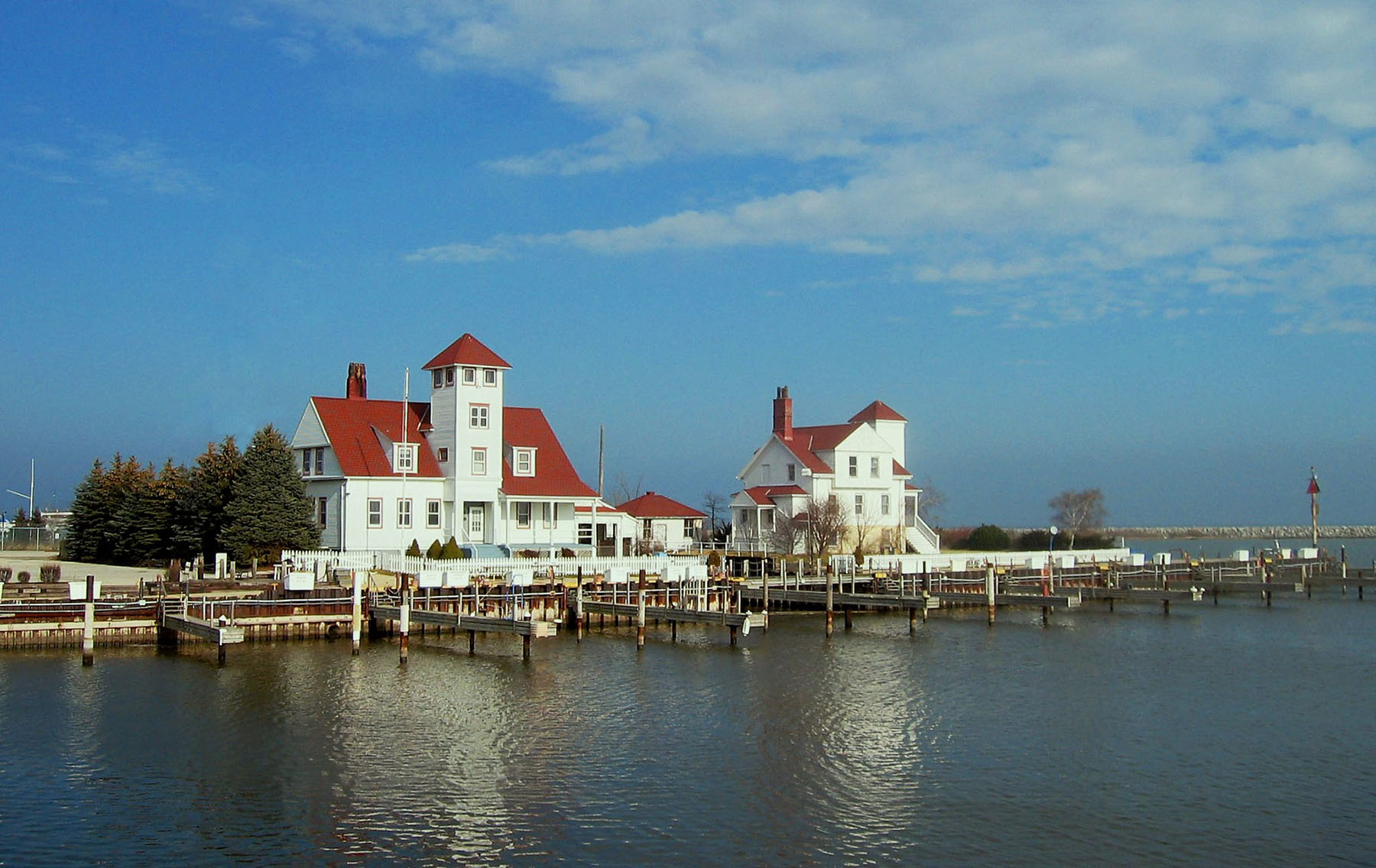 Root River Racine photo by Jeremy Atherton A harbor in Racine, Wisconsin that focuses on two white buildings with red roofs. Lake Michigan is seen in the bottom of the photo, and dark wispy clouds are in the sky in the top center and right.
